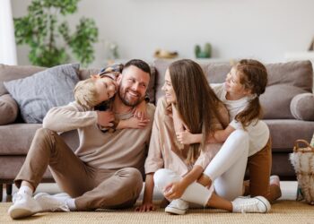 Fröhliche Eltern sitzen mit zwei Kindern vor dem Sofa