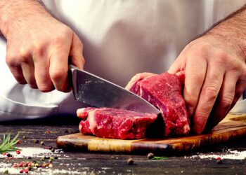 Ein Mann schneidet ein Stück Fleisch auf einem Holzbrett.