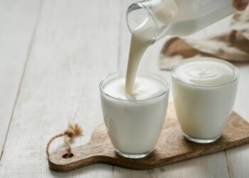 Pouring homemade kefir, buttermilk or yogurt with probiotics. Yogurt flowing from glass bottle on white wooden background. Probiotic cold fermented dairy drink. Trendy food and drink. Copy space left (Bild:  fascinadora/stock.adobe.com)