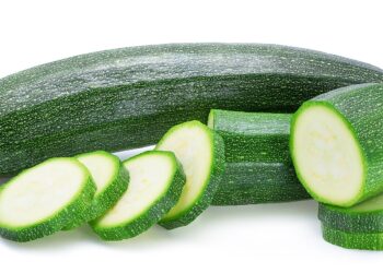 Zucchini und Zucchini-Scheiben vor weißem Hintergrund