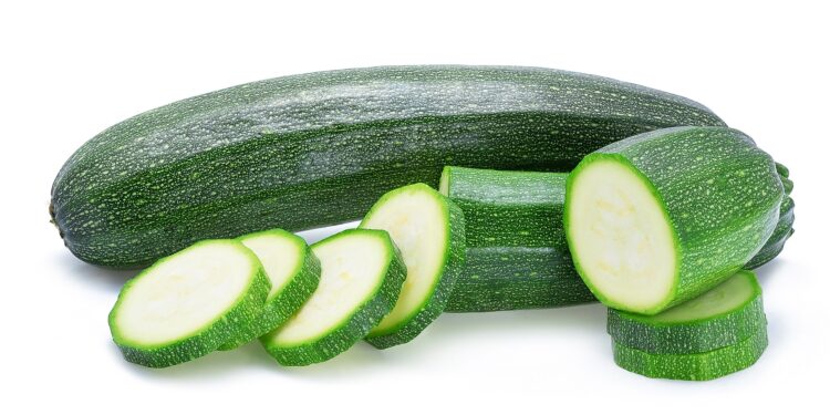 Zucchini und Zucchini-Scheiben vor weißem Hintergrund